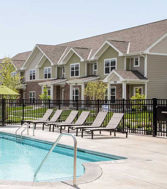 A pool surrounded by lounge chairs and a fence in front of a row of houses. at The Edison at Rice Creek I and II, Minnesota, 55126