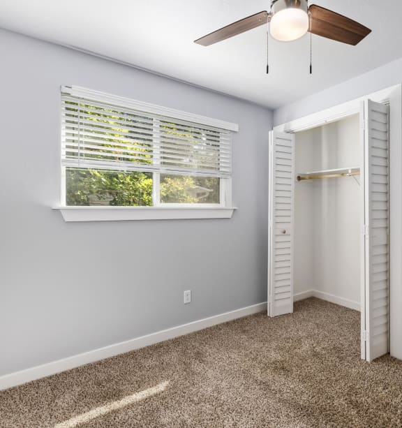 an empty bedroom with a ceiling fan and a window
