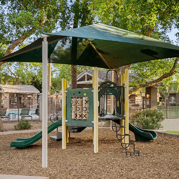 A playground with a green slide and a canopy.