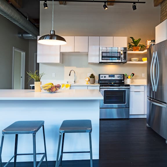 A modern kitchen with a white counter and bar stools.