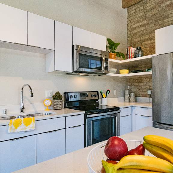 A kitchen with a white counter top and a bowl of fruit on it.