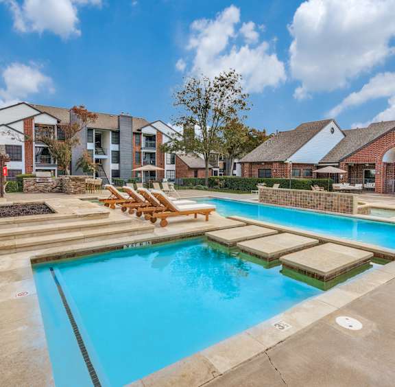 A large outdoor swimming pool with loungers and a building in the background.