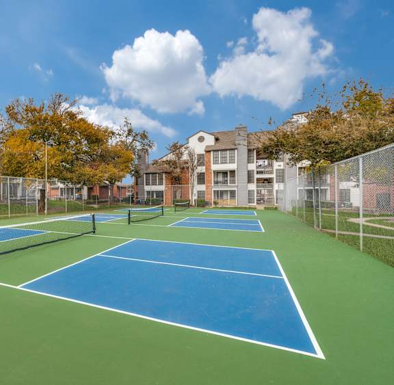 A tennis court surrounded by a fence and buildings.