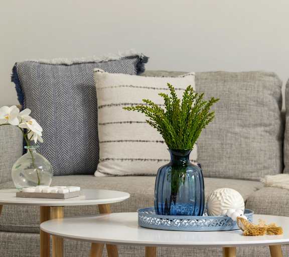 A living room with a grey couch, a white coffee table, and a blue vase with greenery.