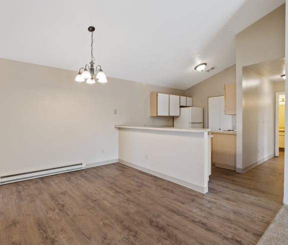 an empty living room and kitchen with wood flooring and white walls