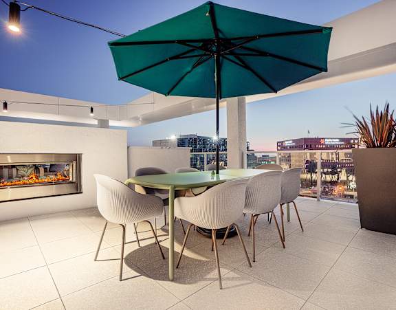 A table with chairs and an umbrella is in the foreground of a cityscape.