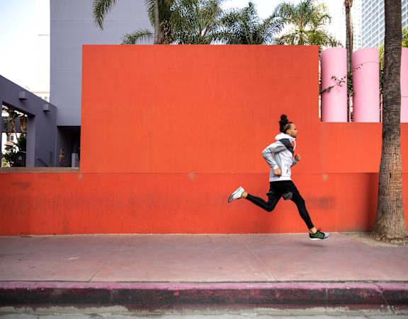 A woman running in front of a bright orange wall.