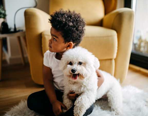 A small child is sitting on the floor holding a white dog.