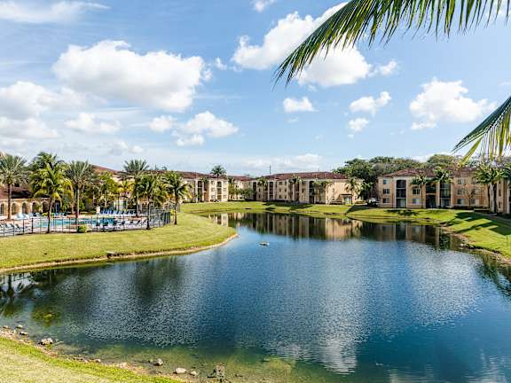 A serene lake surrounded by buildings and palm trees under a clear blue sky.