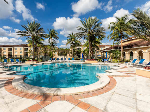 A large outdoor swimming pool surrounded by palm trees and lounge chairs.