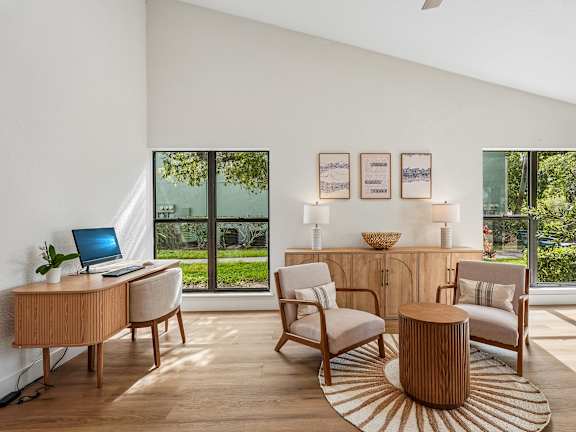 A modern living room with a laptop on the desk and a view of the garden outside.