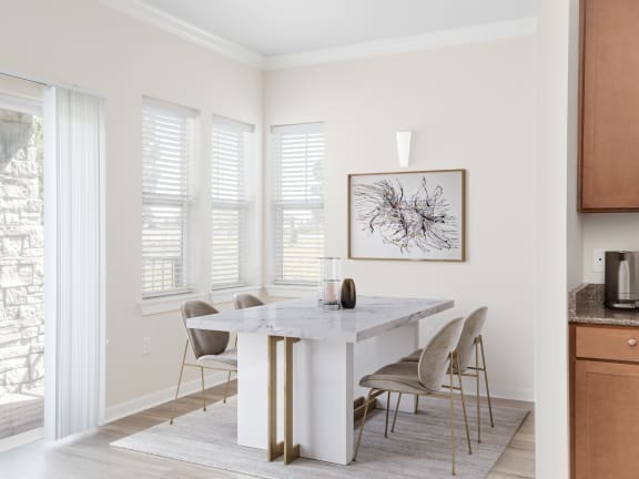 a dining area with a white table and chairs and a large window with white shutters