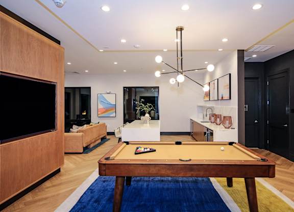 A pool table is in the middle of an apartment clubroom with a TV and a couch.