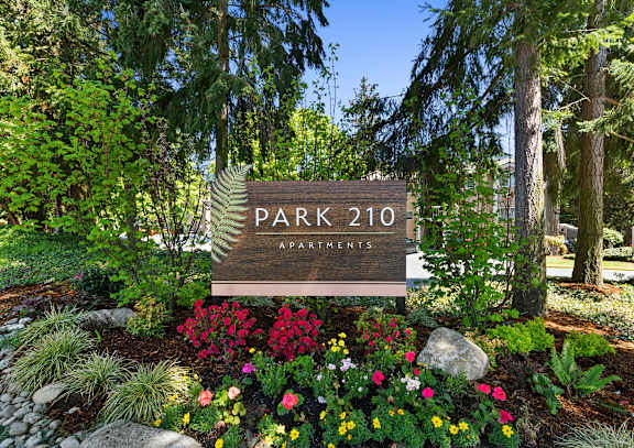 a sign that says park 201 apartments with flowers and trees in front of it  at Park 210 Apartment Homes, Edmonds, Washington