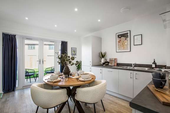 A modern dining room with a table set for two and a kitchen area in the background.