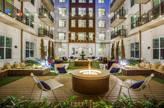 A courtyard with a fire pit surrounded by chairs and plants.