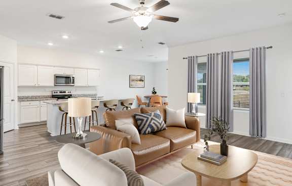 A modern living room with a brown leather couch and a white kitchen in the background.