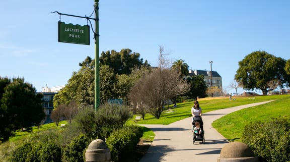 a woman pushing a stroller down a path in a park