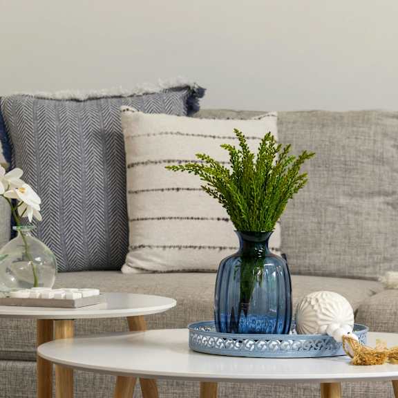 A living room with a grey couch, a white coffee table, and a blue vase with greenery.