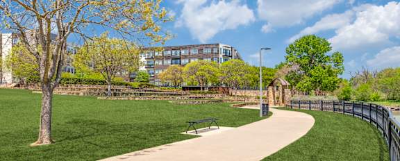 A park with a paved walkway, a bench, and a fence.