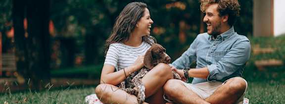A man and woman sitting on the grass with a dog between them.