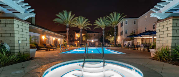 a pool with a hot tub at night at a hotel with palm trees