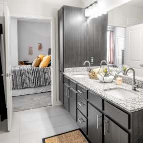 A bathroom with a sink, mirror, and a bedroom in the background.