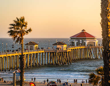 A pier with a red roof and a building on it with people walking on the beach.