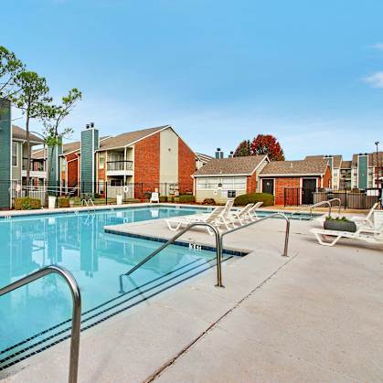A swimming pool surrounded by a concrete floor and metal railings with apartment buildings in the background.