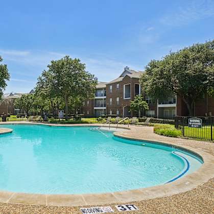A large swimming pool surrounded by trees and apartment buildings.