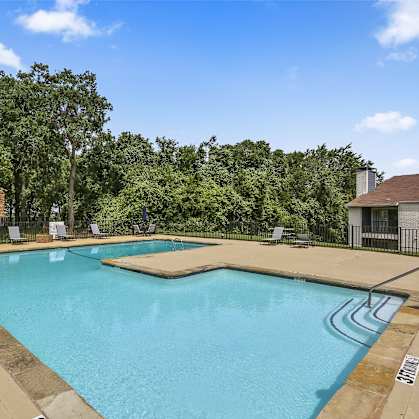 A large outdoor swimming pool surrounded by trees and lounge chairs.
