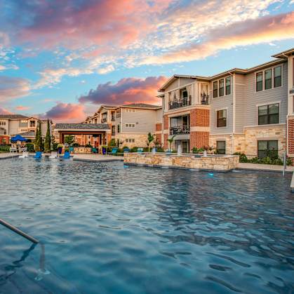 a swimming pool with buildings and a sunset in the background