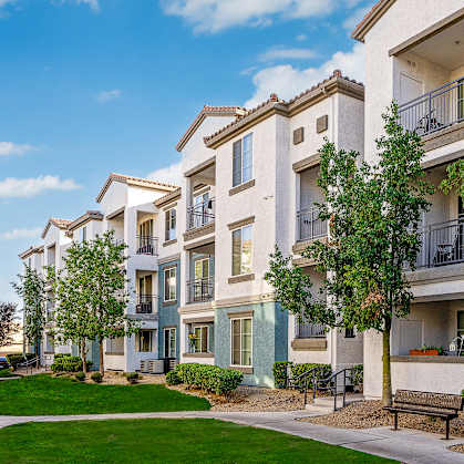 A row of apartment buildings with balconies and trees in front.