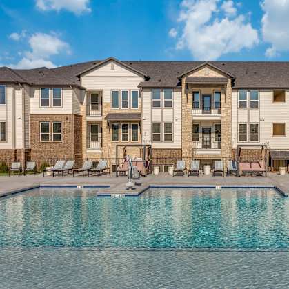 A large swimming pool in front of a building with lounge chairs around it.