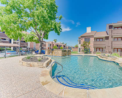 A swimming pool surrounded by a stone patio and a tree.