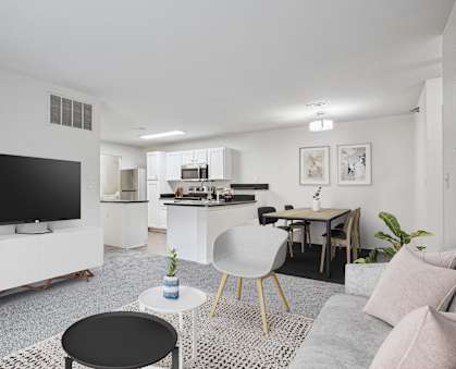 A modern living room with a television, a dining table, and a kitchen area.