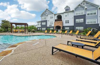 A pool area with sun loungers and a building in the background.
