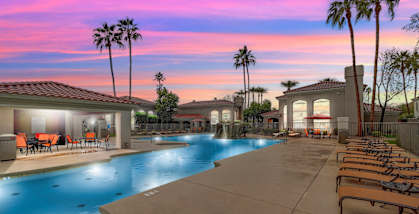 A swimming pool with lounge chairs and palm trees.