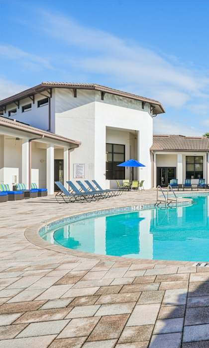 A swimming pool surrounded by a tiled patio and a white building with a balcony.