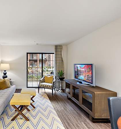 A living room with a grey couch, a yellow cushion, a wooden coffee table, a television, and a painting on the wall at MainCentre, Michigan, 48167