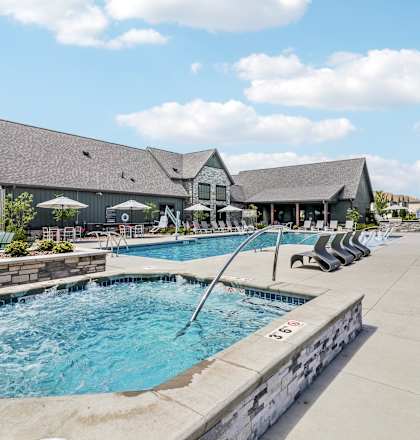 a swimming pool with chairs and a building in the background at The Depot Luxury Apartment Homes, Raymore, MO, 64083