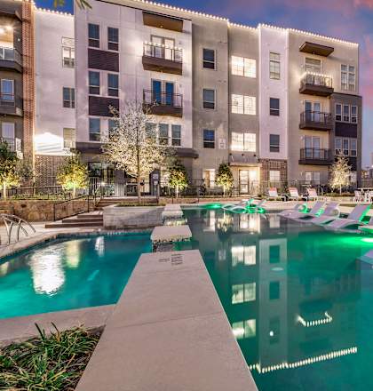 A swimming pool in front of a building with lights around it.