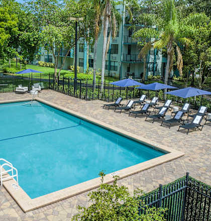 a swimming pool with lounge chairs and umbrellas in front of an apartment building  at Club at Emerald Waters, Hollywood, FL