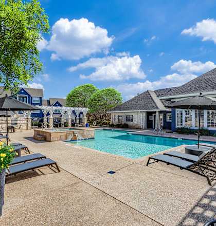 A pool area with sun loungers and a tree.