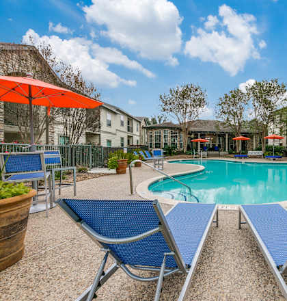 a swimming pool with blue chairs and umbrellas and apartments in the background at Sunrise Canyon, Universal City, TX, 78148
