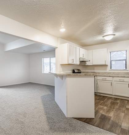 A spacious, empty room with a kitchenette and a large window with a view of a balcony.