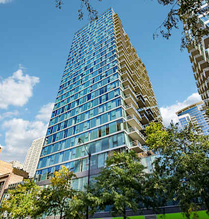 A tall building with many windows stands in front of other buildings and trees.
