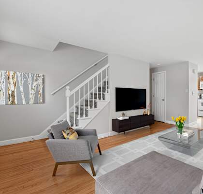 A living room with a grey couch, a grey armchair, a glass coffee table and a television.