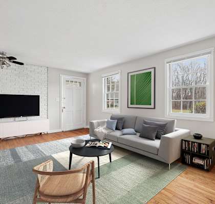 A living room with a grey couch, a black coffee table, a white television, a ceiling fan, and a green rug.