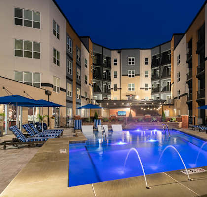 a swimming pool at night at an apartment building with a blue lighted pool at Aster Apartments, Ohio, 44122
